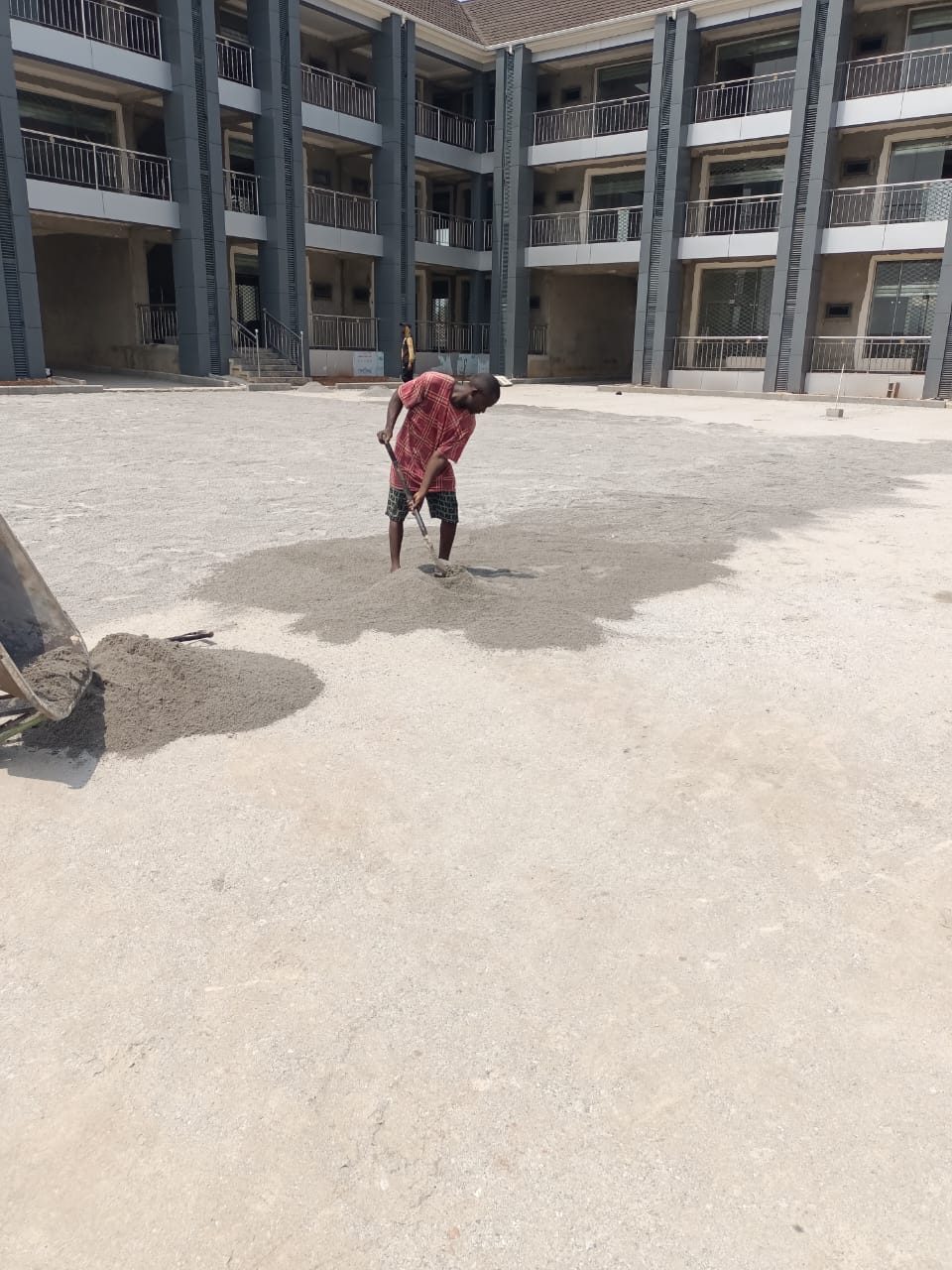 Worker levelling laterite fill in the courtyard of an institutional building development