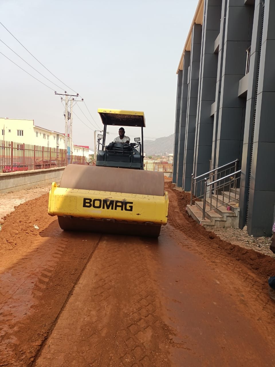 Roller compacting laterite fill beside an institutional building