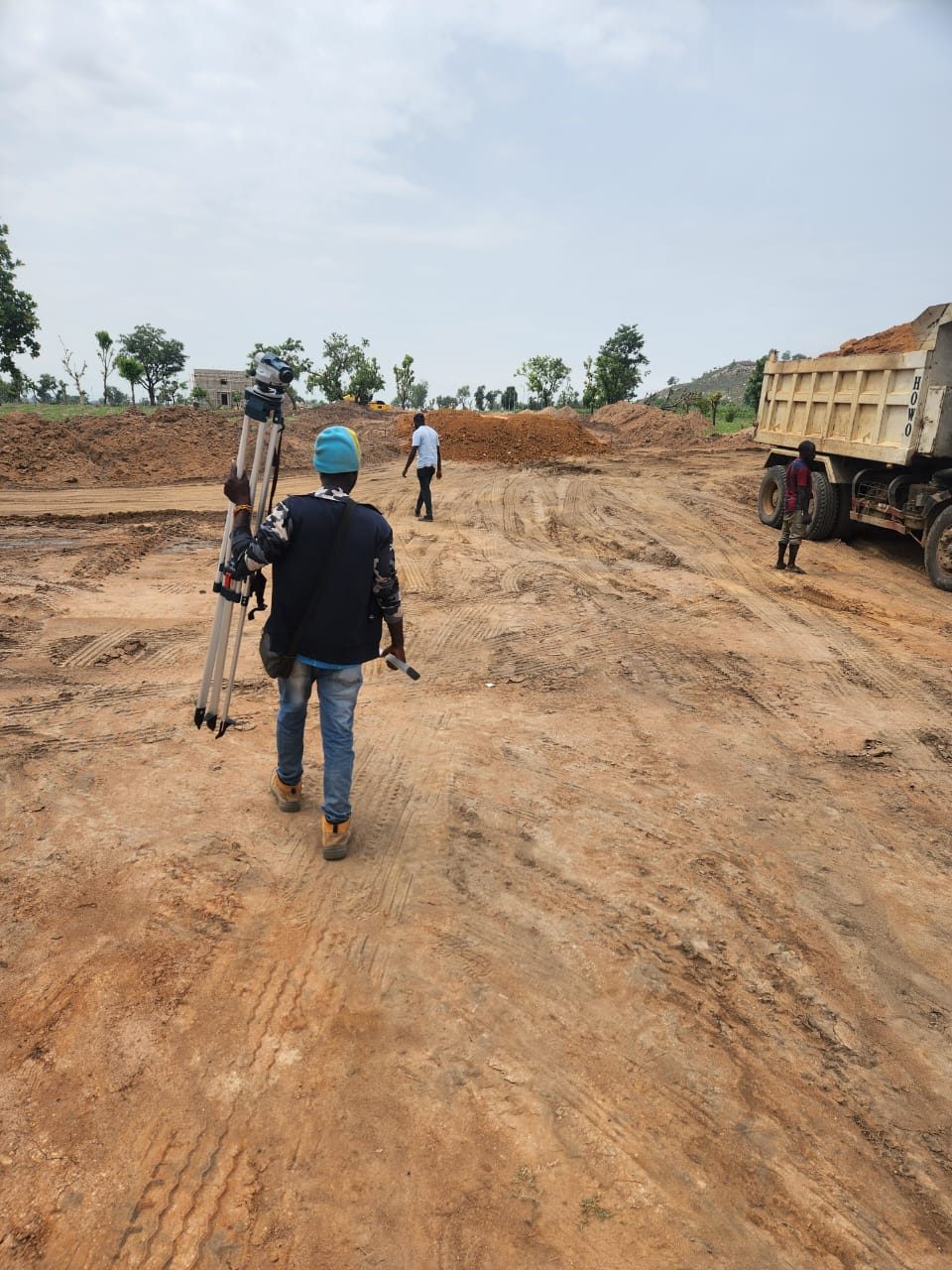 Surveyor carrying equipment across an active earthworks site, Abuja
